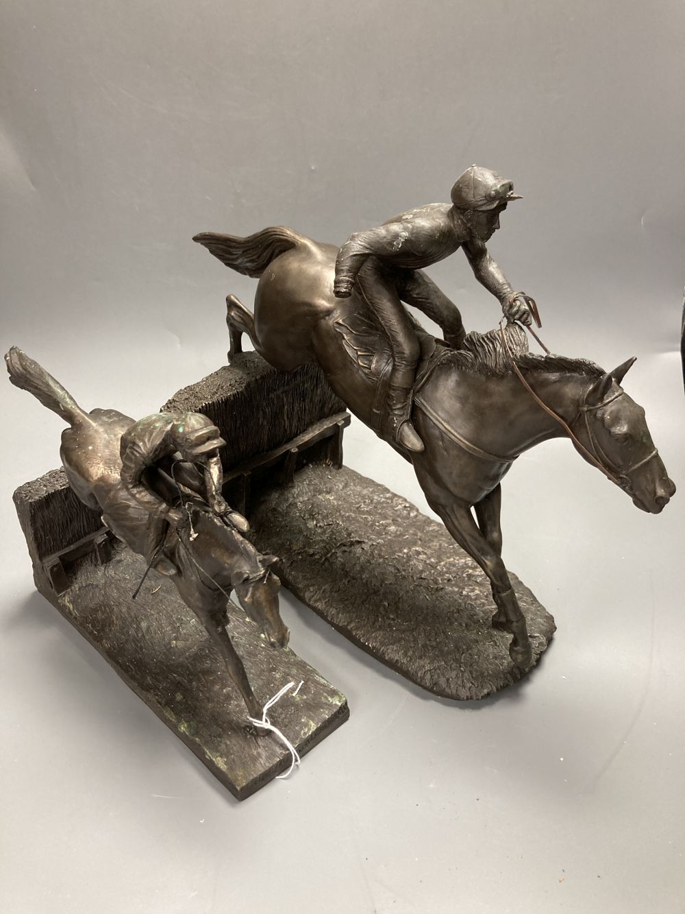 Two bronzed resin models of a steeplechasers, taking a fence, widest 35cm